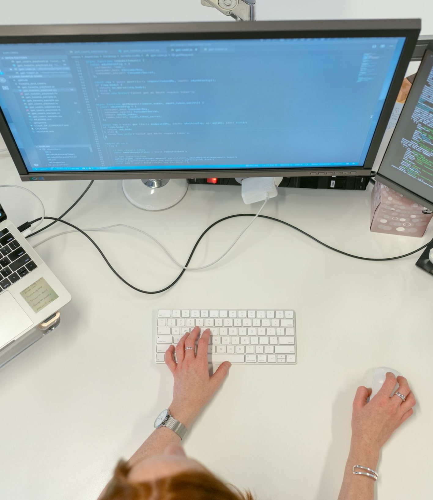 Two monitors and a laptop showing data on a work desk