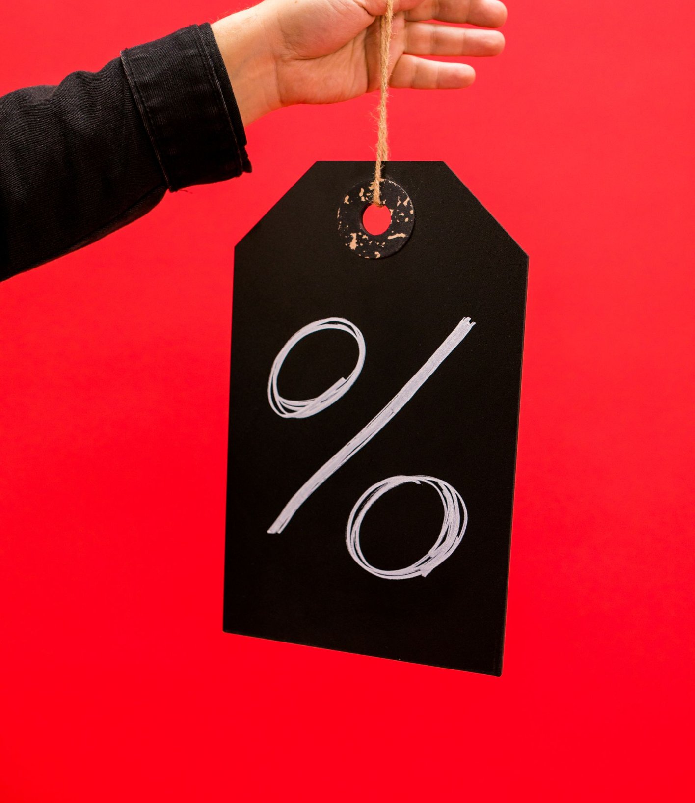 Hand holding a black tag with a percent sign on a red background