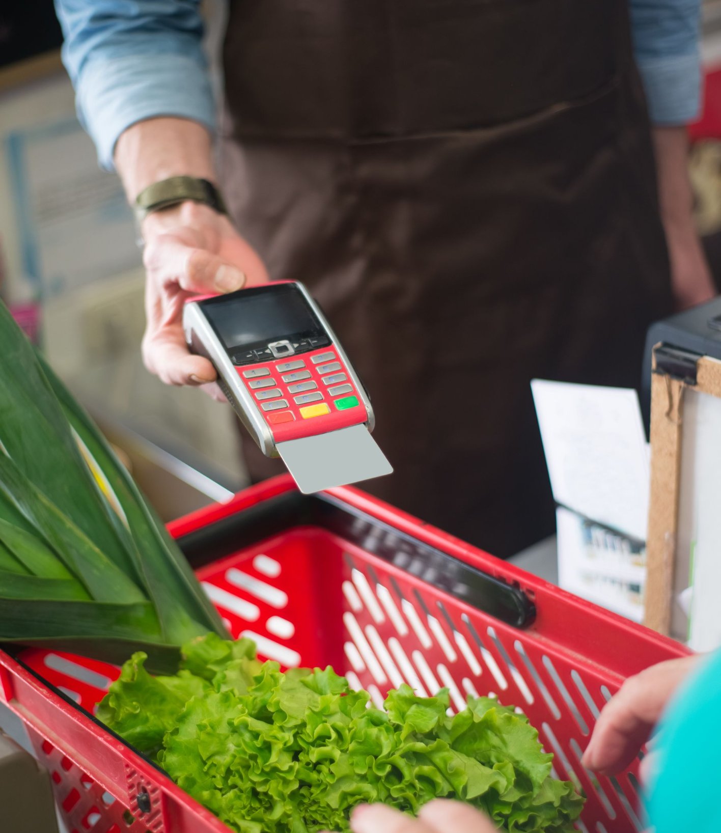 Shopper paying by card at a supermarket checkout with a basket of vegetables